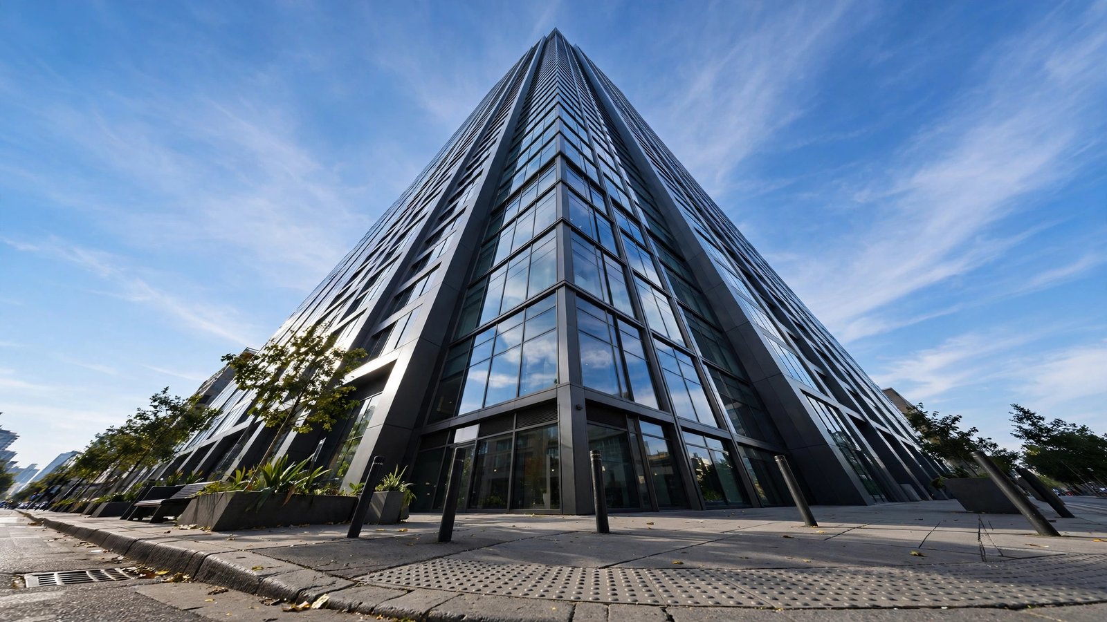 Dramatic low-angle view looking up at a modern glass skyscraper against a bright blue sky with wispy clouds